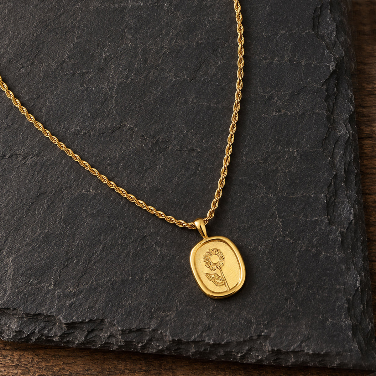 Nahaufnahme des goldenen Blumenmedaillons mit poliertem Rand und gedrehter Kordelkette auf Schiefer