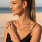 Gold-tone jewelry set with pearl necklace, sun pendant and matching pearl bracelet on a white background